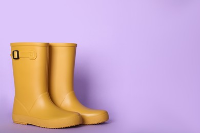Photo of Yellow rubber boots on violet background. Space for text