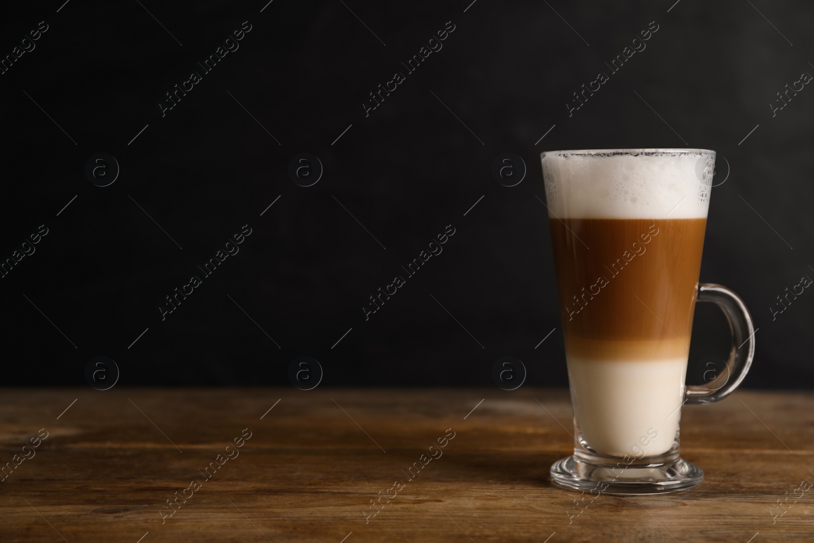 Photo of Hot coffee with milk in glass cup on wooden table. Space for text