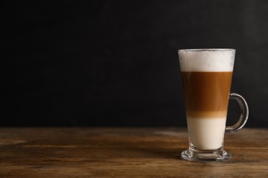 Hot coffee with milk in glass cup on wooden table. Space for text