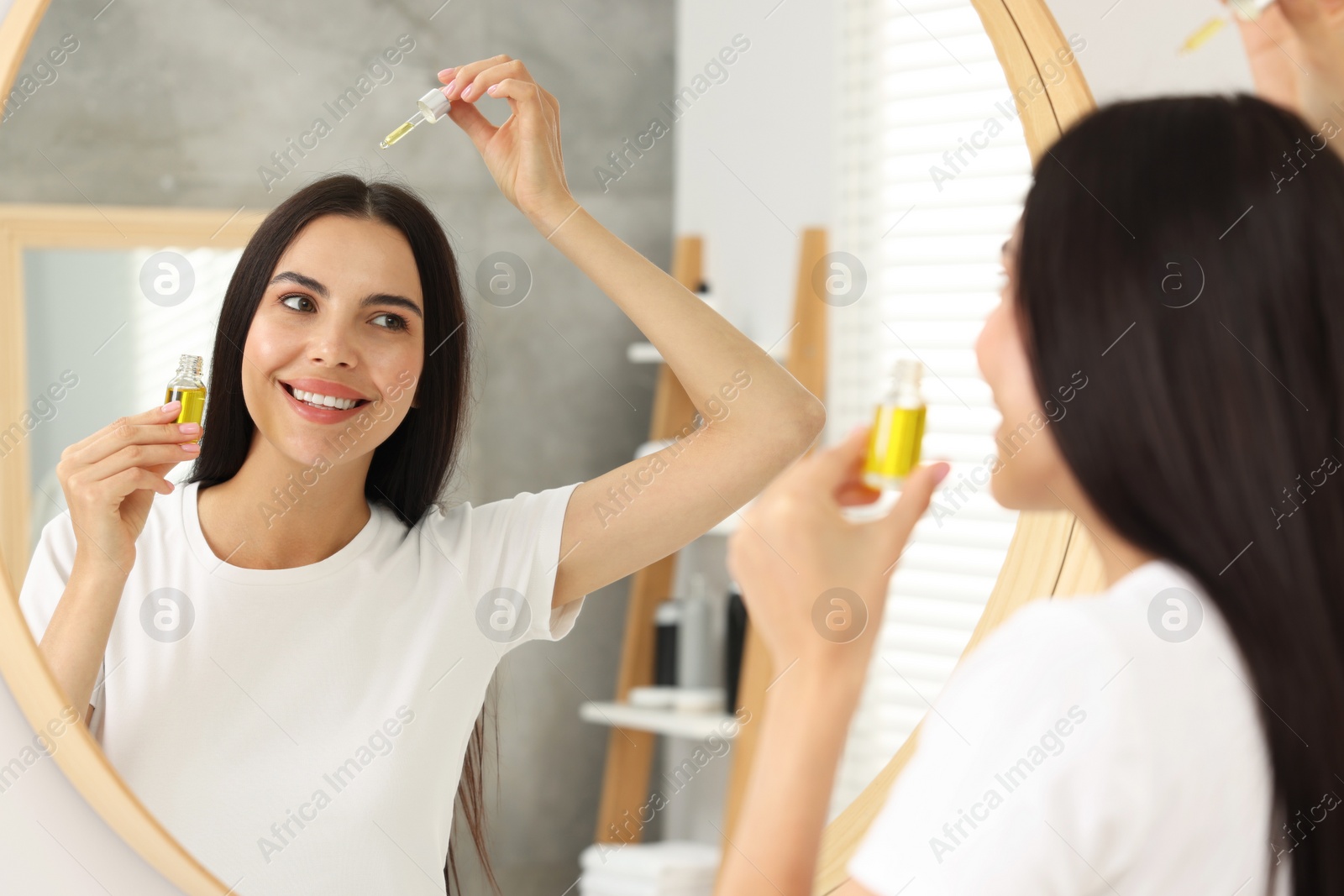 Photo of Beautiful woman applying hair serum in bathroom. Cosmetic product