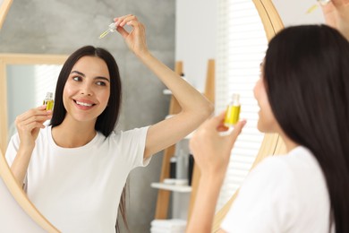 Beautiful woman applying hair serum in bathroom. Cosmetic product