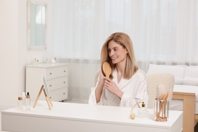 Photo of Beautiful woman brushing her hair at vanity in bedroom