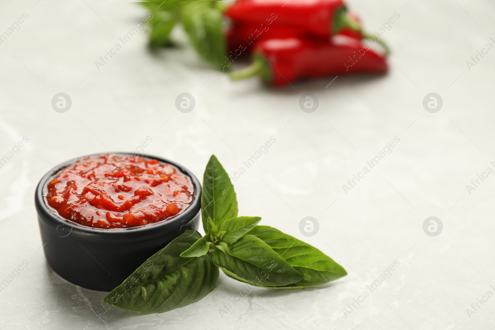 Photo of Delicious adjika sauce in bowl with basil on light marble table, closeup. Space for text