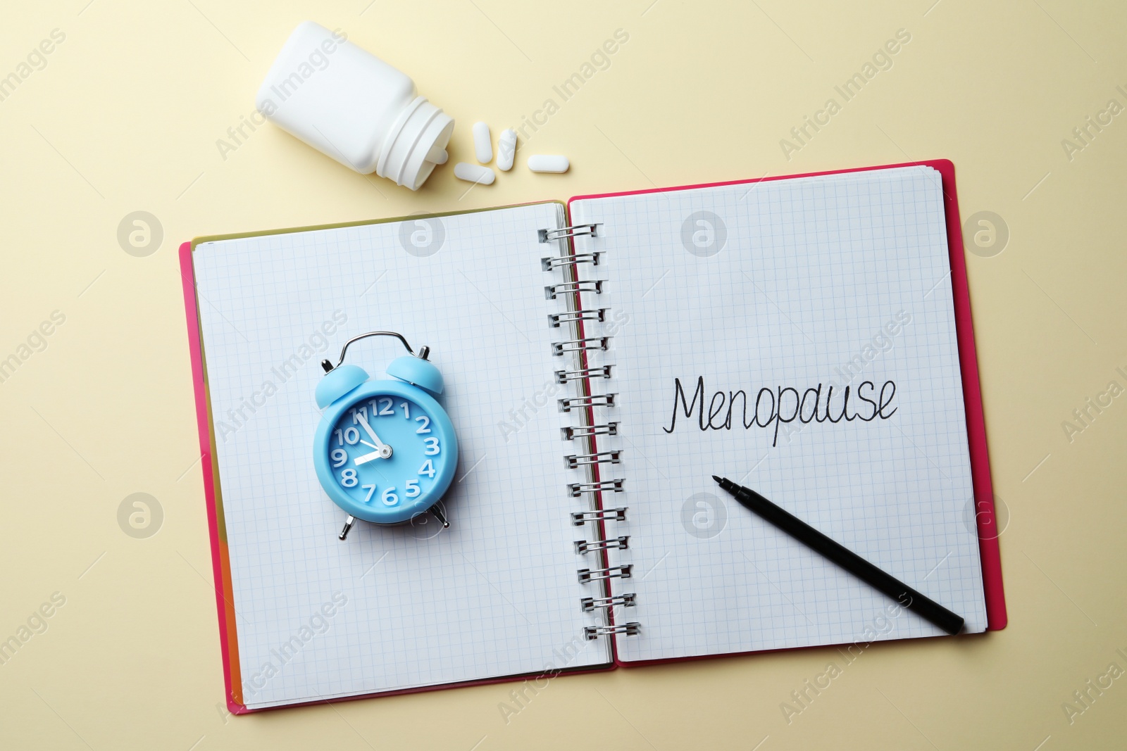 Photo of Notebook with word Menopause, alarm clock, pills and marker on beige background, flat lay