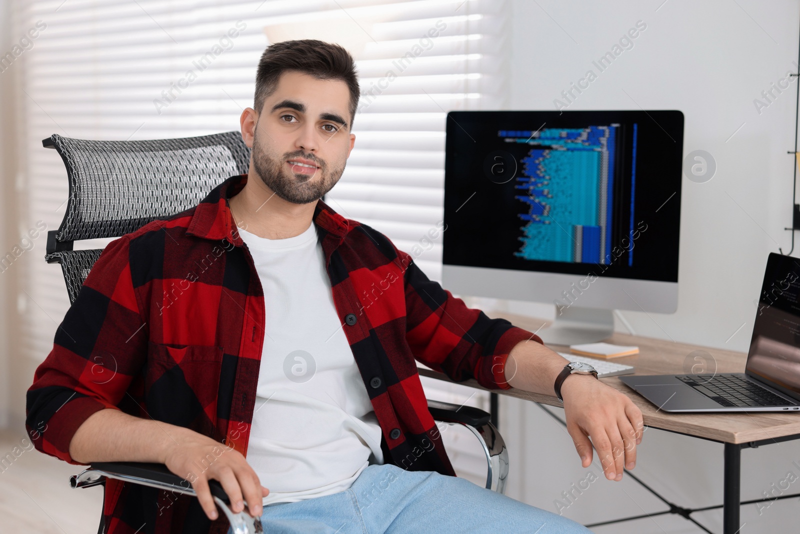 Photo of Happy young programmer working at desk in office