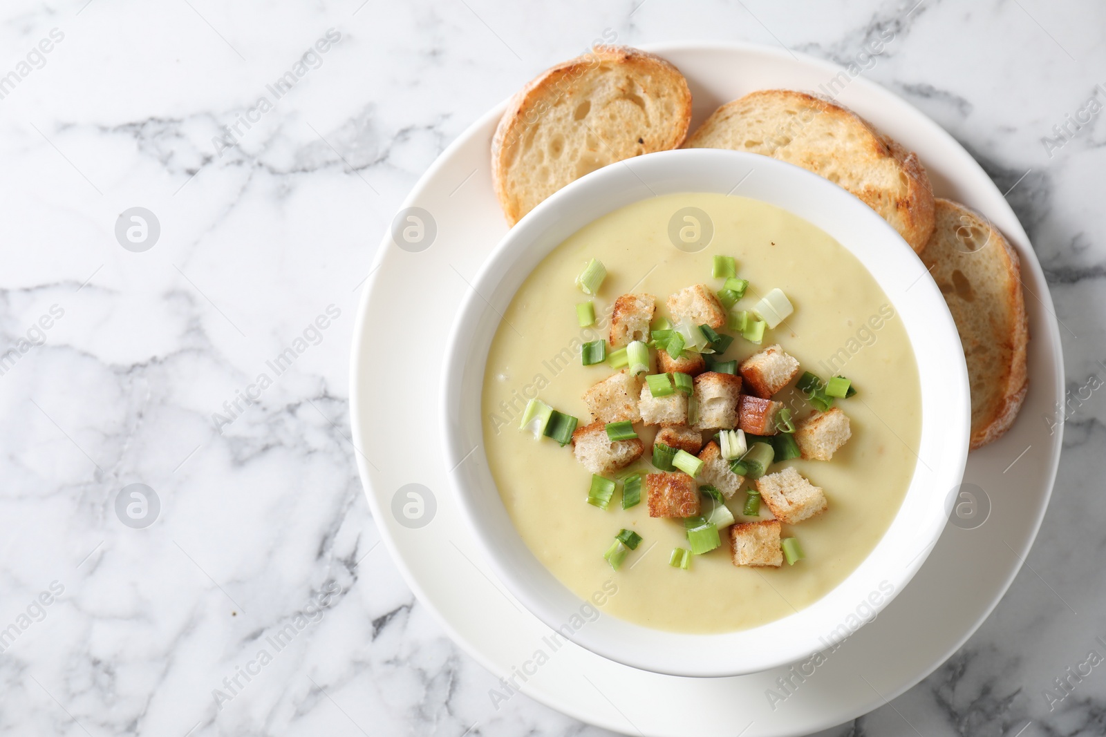 Photo of Tasty potato soup with croutons and green onion in bowl on white marble table, top view. Space for text