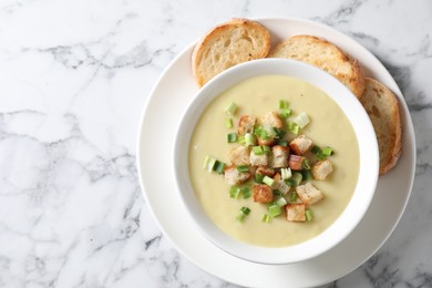 Photo of Tasty potato soup with croutons and green onion in bowl on white marble table, top view. Space for text