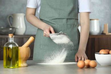 Photo of Woman sieving flour at table in kitchen, closeup