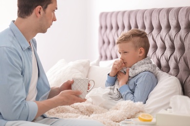 Photo of Father taking care of little son suffering from cold in bed