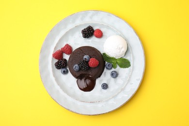Photo of Delicious chocolate fondant served with fresh berries and ice cream on yellow background, top view