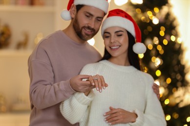 Photo of Making proposal. Happy woman with engagement ring and her fiance at home on Christmas, selective focus