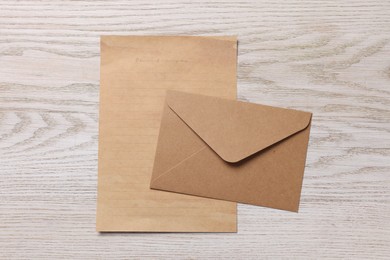 Photo of Envelope and sheet of parchment paper on white wooden table, flat lay