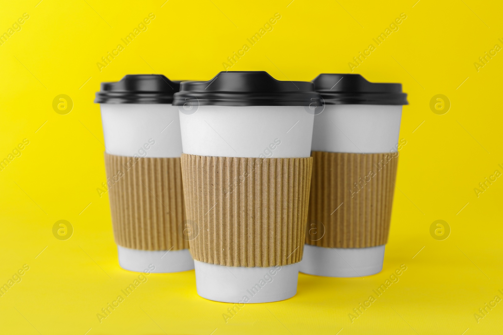 Photo of Paper cups with black lids on yellow background. Coffee to go