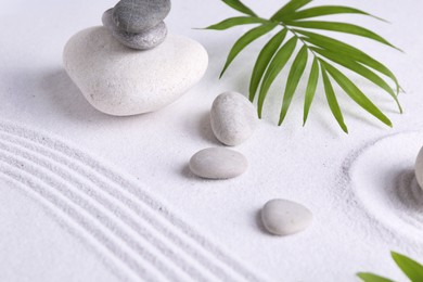 Photo of Zen garden stones and green leaves on white sand with pattern