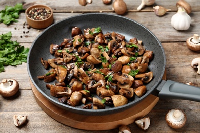 Photo of Frying pan with mushrooms on wooden table