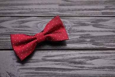 Stylish burgundy bow tie with polka dot pattern on wooden table, top view. Space for text