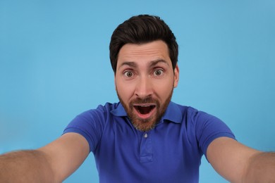 Emotional man taking selfie on light blue background