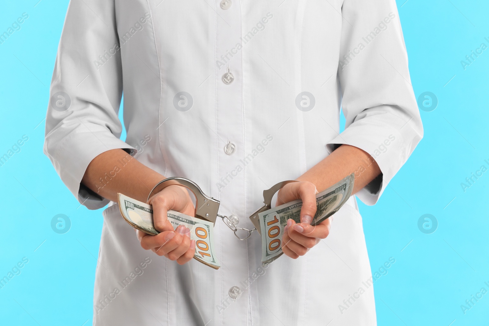 Photo of Doctor in handcuffs with bribe on light blue background, closeup. Corrupted medicine