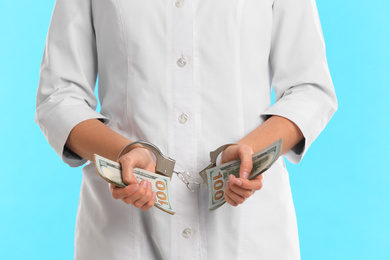 Doctor in handcuffs with bribe on light blue background, closeup. Corrupted medicine