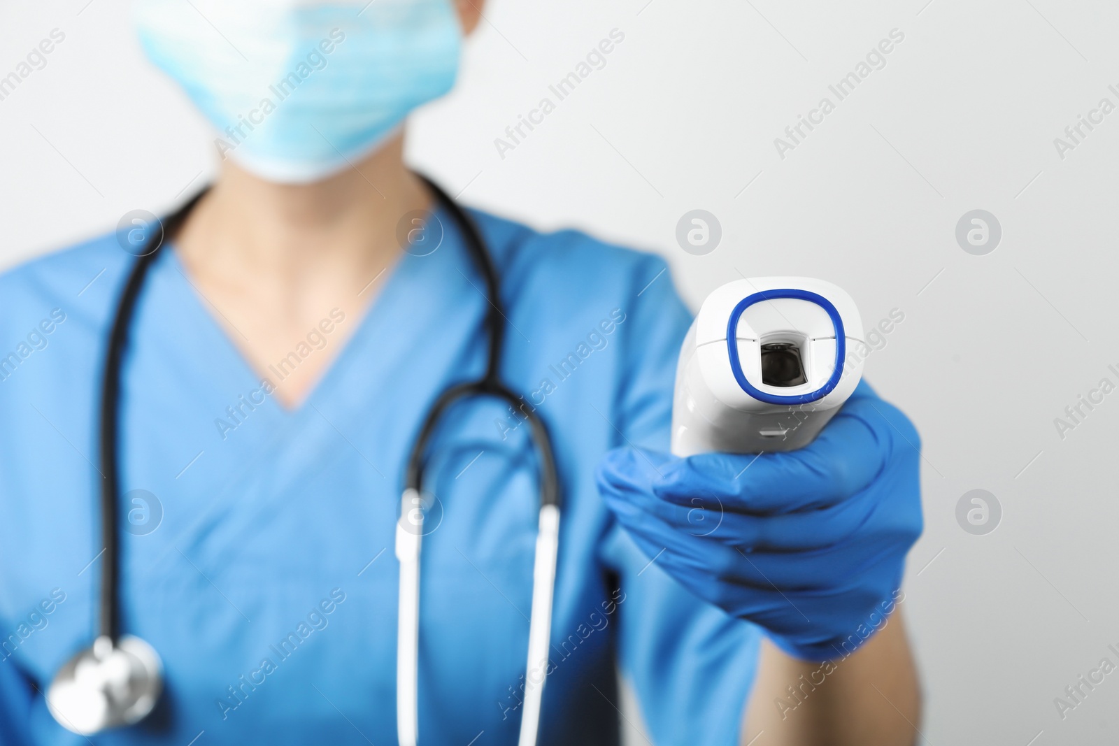 Photo of Doctor with infrared thermometer on light background, closeup. Checking temperature during Covid-19 pandemic