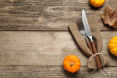 Photo of Cutlery, napkin and pumpkins on wooden background, flat lay with space for text. Table setting