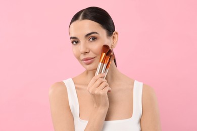 Beautiful woman with different makeup brushes on pink background