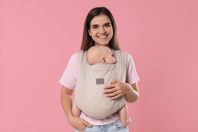 Mother holding her child in sling (baby carrier) on pink background