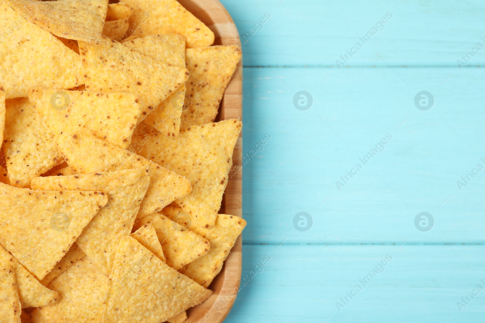 Photo of Wooden plate of tasty Mexican nachos chips on light blue wooden background, top view. Space for text
