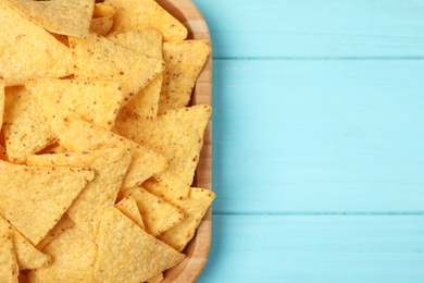 Wooden plate of tasty Mexican nachos chips on light blue wooden background, top view. Space for text