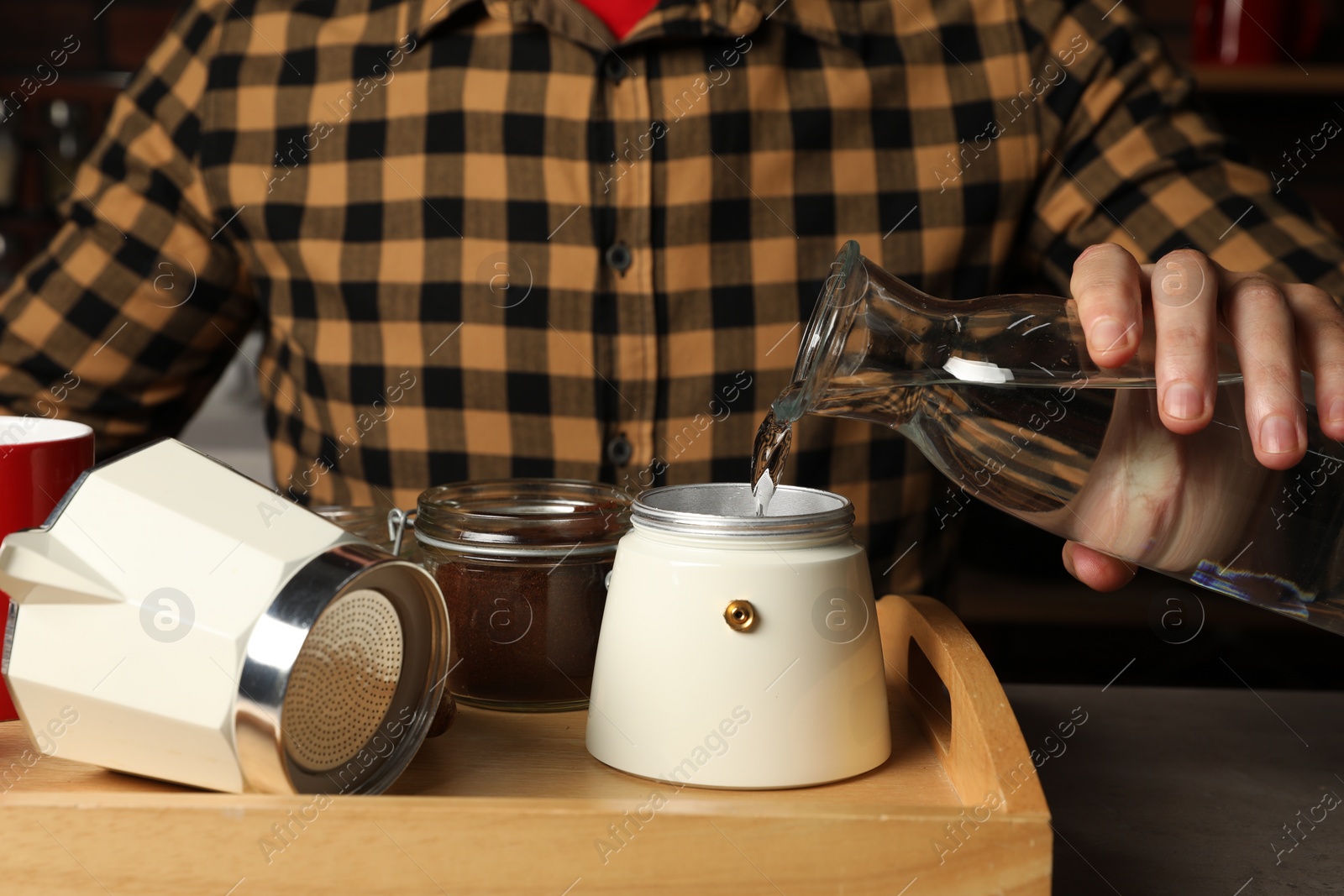Photo of Brewing coffee. Man pouring water into moka pot at table indoors, closeup