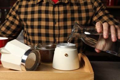 Brewing coffee. Man pouring water into moka pot at table indoors, closeup