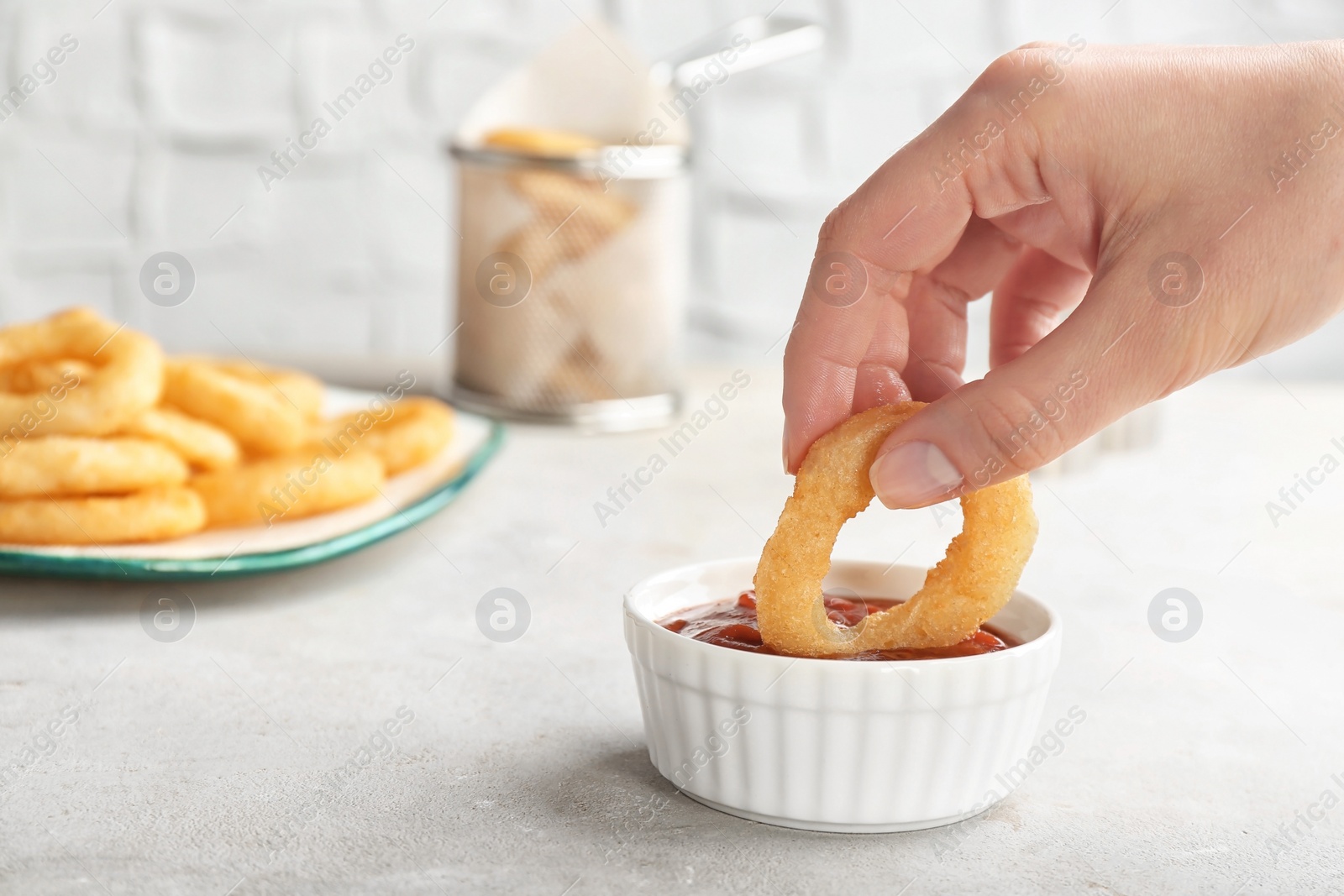 Photo of Woman dipping tasty onion ring into bowl with ketchup on table