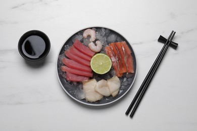 Photo of Sashimi set (raw slices of tuna, oily fish, salmon, and shrimps) served with lime, soy sauce and ice on white marble table, flat lay