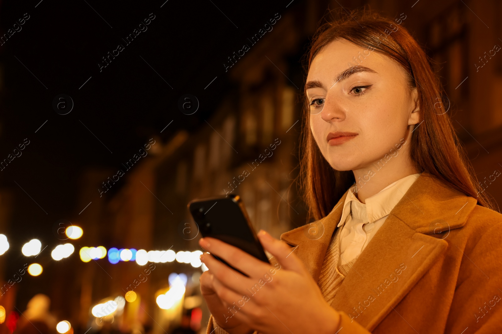 Photo of Beautiful woman using smartphone on night city street. Space for text