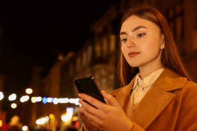 Photo of Beautiful woman using smartphone on night city street. Space for text