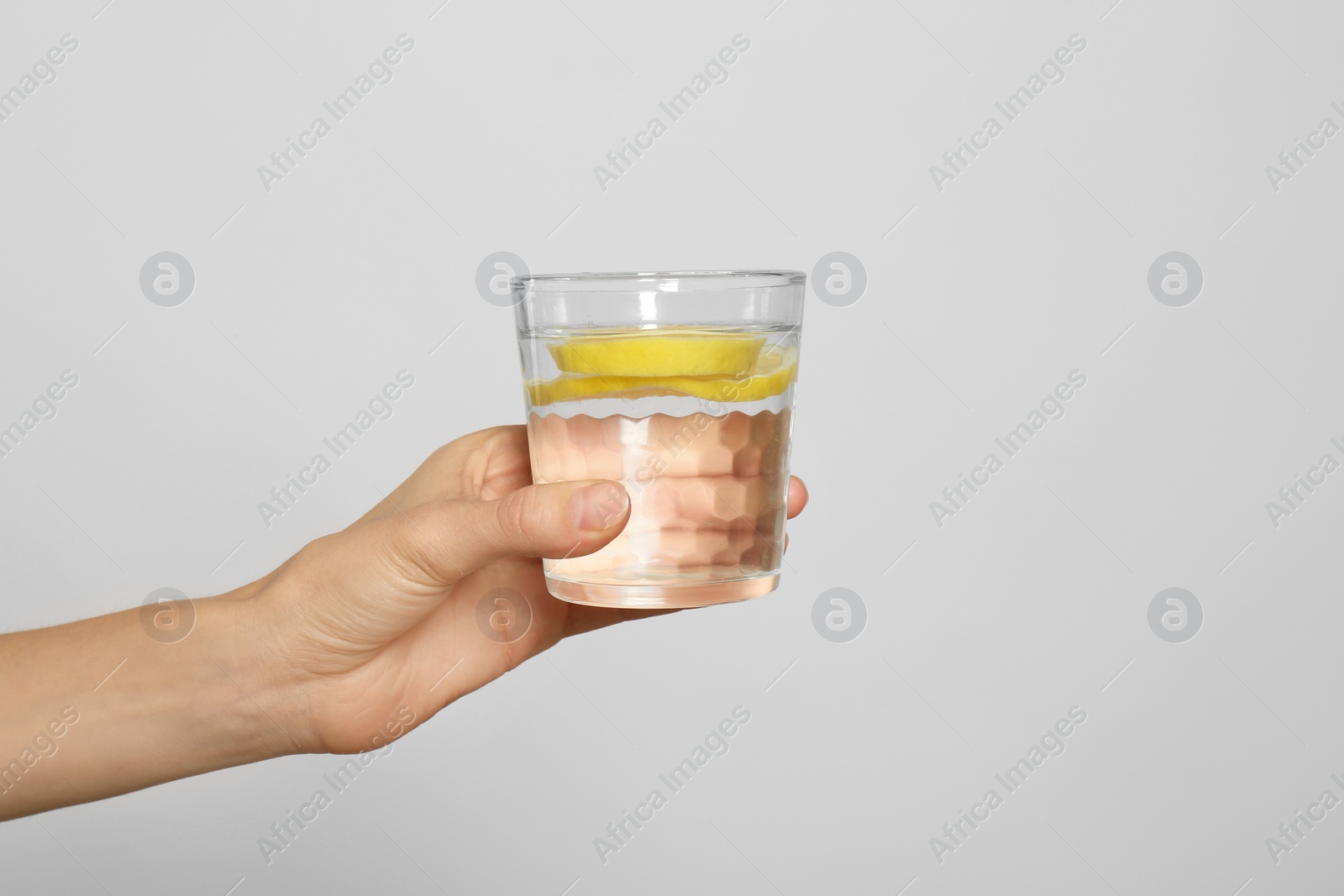 Photo of Young woman with glass of lemon water on light background, closeup