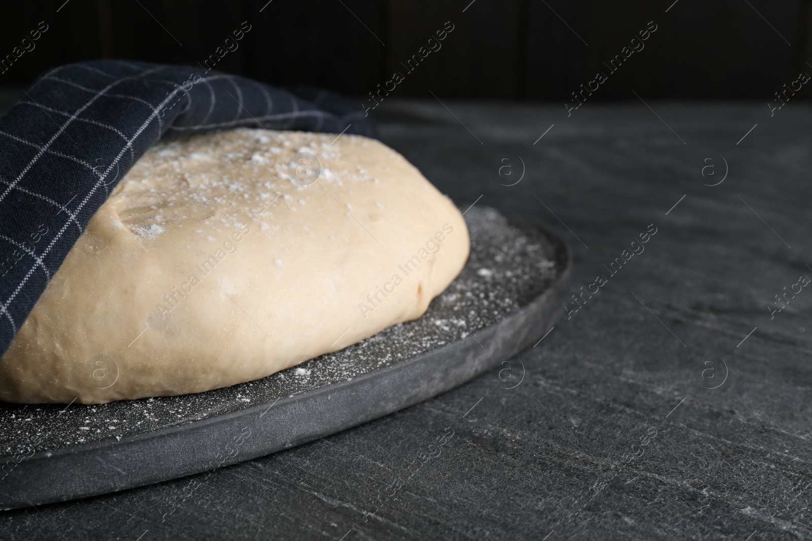 Photo of Fresh yeast dough with flour on black table. Space for text