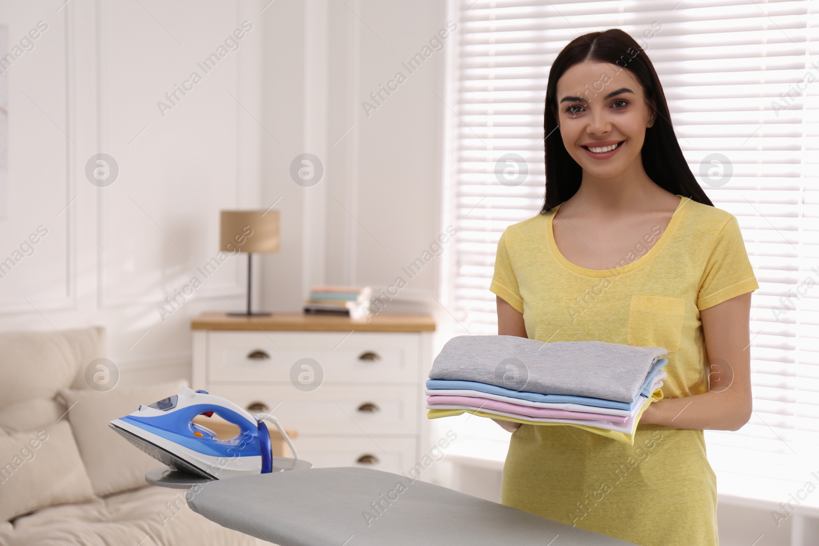 Photo of Woman with folded clothes near ironing board at home. Space for text