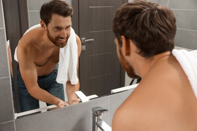 Photo of Handsome bearded man looking at mirror in bathroom near wooden doors