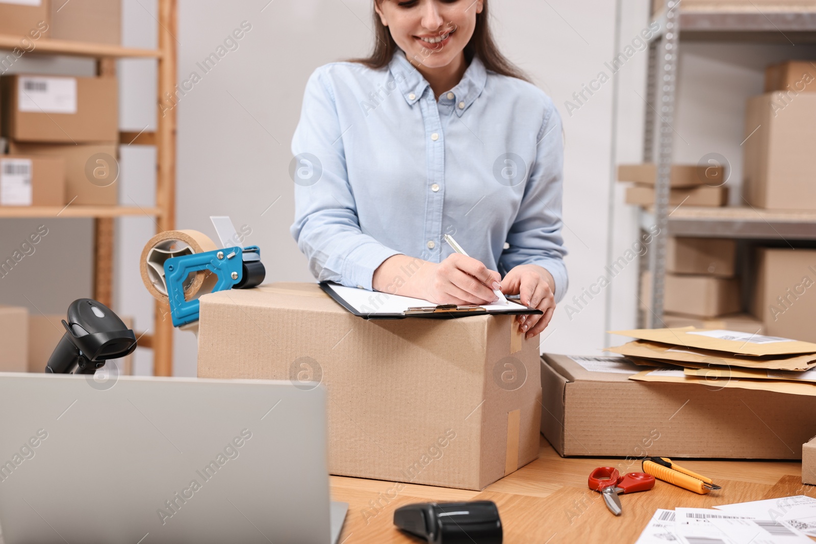 Photo of Parcel packing. Post office worker with clipboard writing notes at wooden table indoors