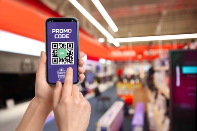 Woman holding smartphone with activated promo code in shopping mall, closeup