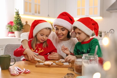 Photo of Mother and her cute little children decorating tasty Christmas cookies at table in kitchen