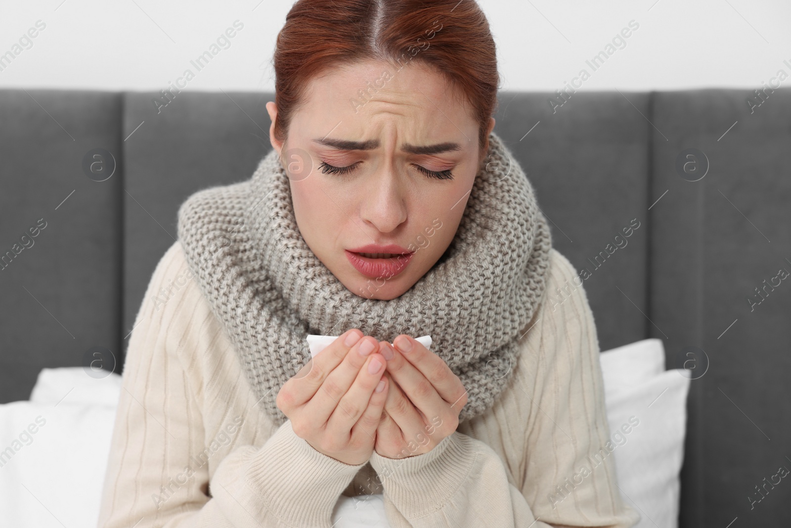 Photo of Woman with tissue coughing on bed. Cold symptoms