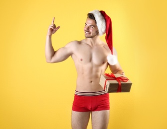 Shirtless sexy young Santa Claus with gift on color background