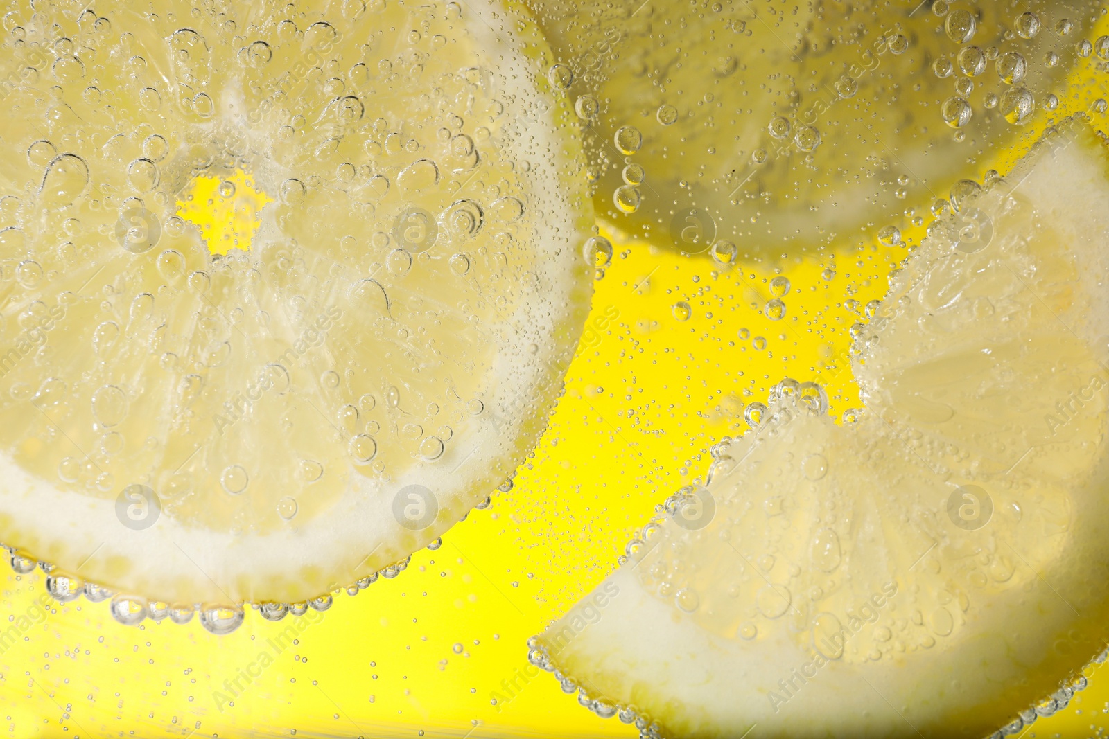 Photo of Juicy lemon slices in soda water against yellow background, closeup