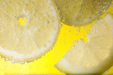 Photo of Juicy lemon slices in soda water against yellow background, closeup