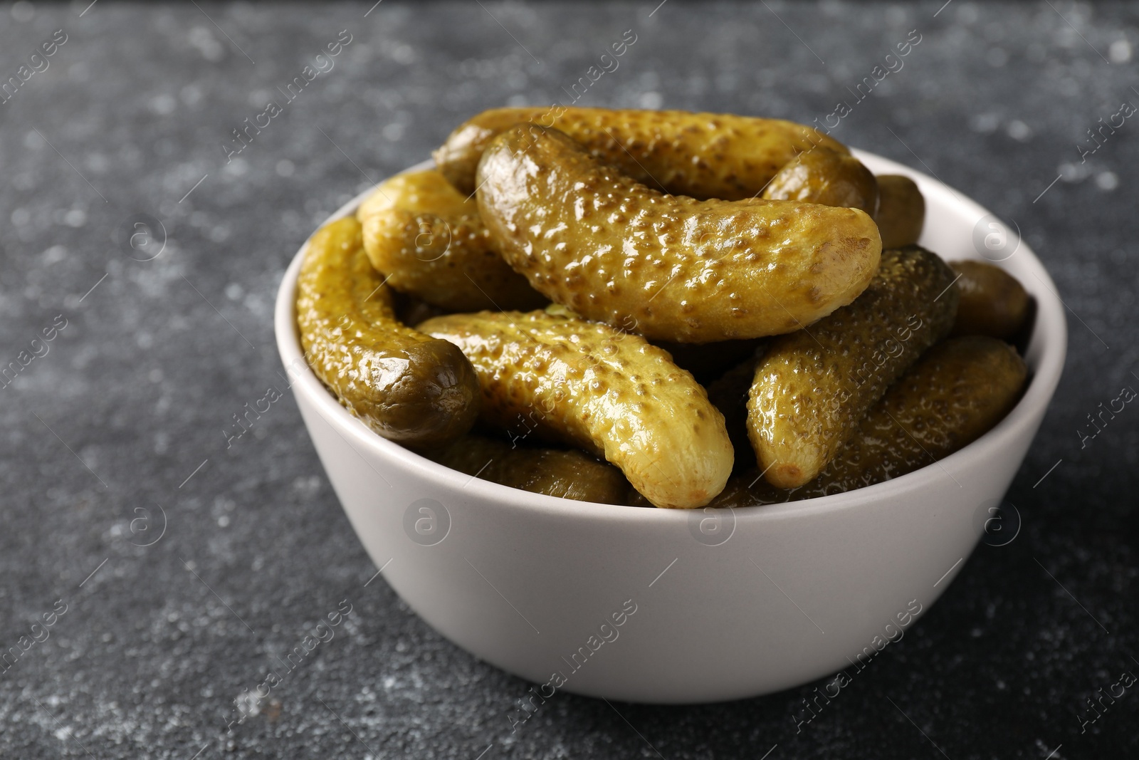 Photo of Tasty pickled cucumbers in bowl on grey table, closeup