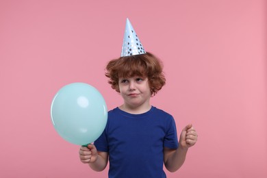 Photo of Sad little boy in party hat with blower on pink background