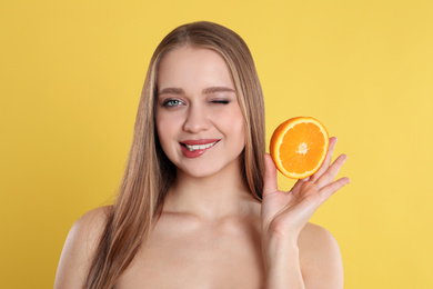 Photo of Young woman with cut orange on yellow background. Vitamin rich food