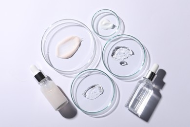 Photo of Petri dishes with samples of cosmetic serums and bottles on white background, flat lay